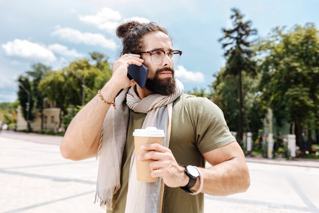 Buen hombre serio poniendo un teléfono en la oreja mientras realiza una llamada telefónica