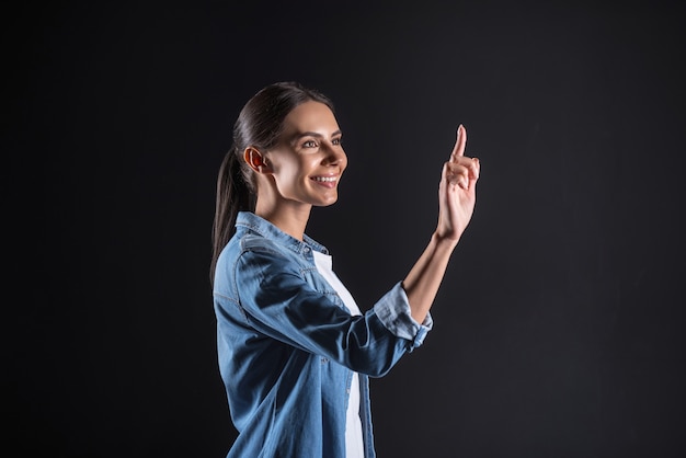 Buen humor. Feliz mujer positiva encantada presionando su dedo a la pantalla sensorial y sonriendo mientras usa tecnología moderna