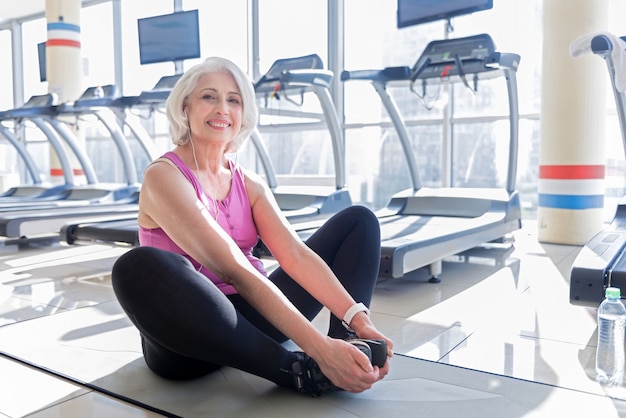 De buen humor. Mujer senior bastante activa sonriendo y haciendo ejercicios en un gimnasio mientras escucha música.