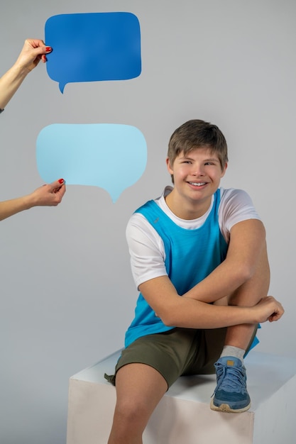 Buen humor. Niño sonriente con camiseta azul sentado y mirando contento