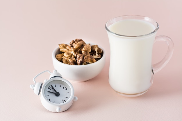 Buen sueño. Alimentos para dormir bien: leche, nueces y despertador sobre fondo rosa