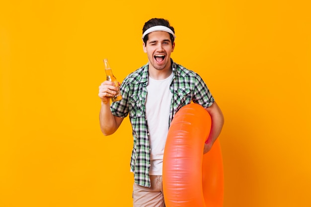 Buen tipo en traje de verano guiños tiene cerveza y anillo de goma sobre fondo naranja