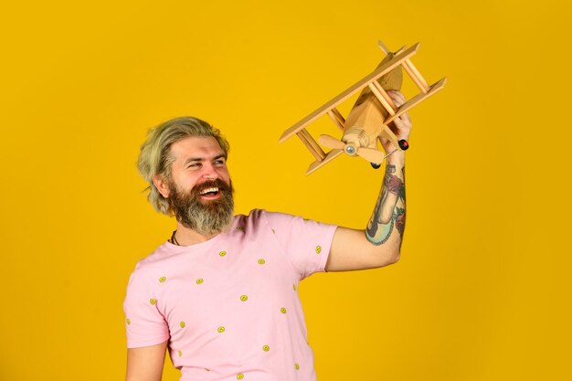 Buen viaje aeromodelismo tienda de juguetes hechos a mano vamos a volar sentir la libertad carpintero feliz hombre barbudo jugar con avión de madera soñar con vacaciones de verano piloto maduro fondo naranja