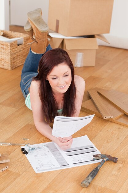 Buena chica pelirroja leyendo un manual antes de bricolaje mientras está acostado en el piso