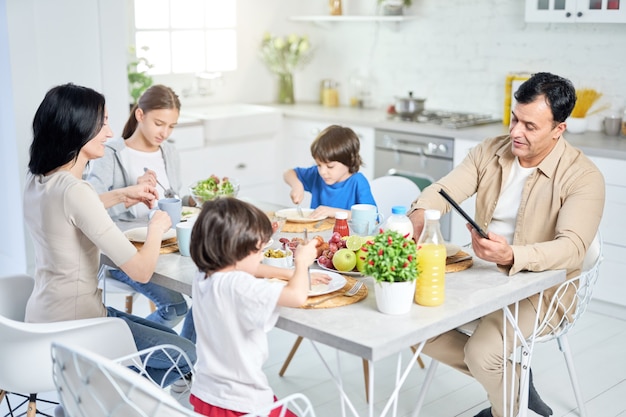 Buena comida alegre familia hispana disfrutando de la comida juntos mientras se desayuna sentado en la mesa