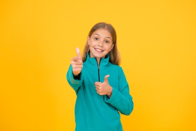 Buena elección Niña feliz apuntando con el arma gesto con la mano Apuntar y apuntar Niño pequeño sonriendo y señalando el fondo amarillo Señalar el gesto como comunicación no verbal Señalar y apuntar