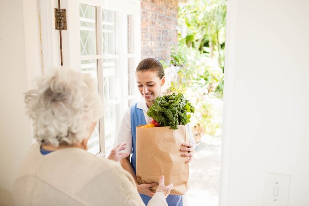 Buena enfermera llevando verduras a un paciente viejo en casa