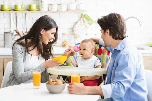 Buena familia joven desayunando junto con su hijo y dándole de comer