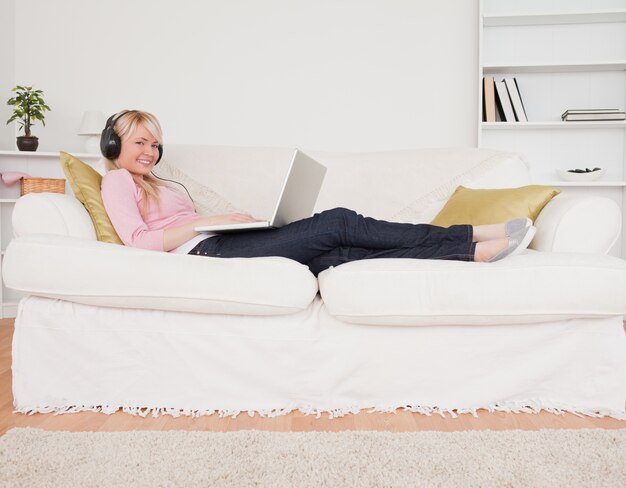 Buena mujer escuchando música en sus auriculares mientras está acostado en un sofá