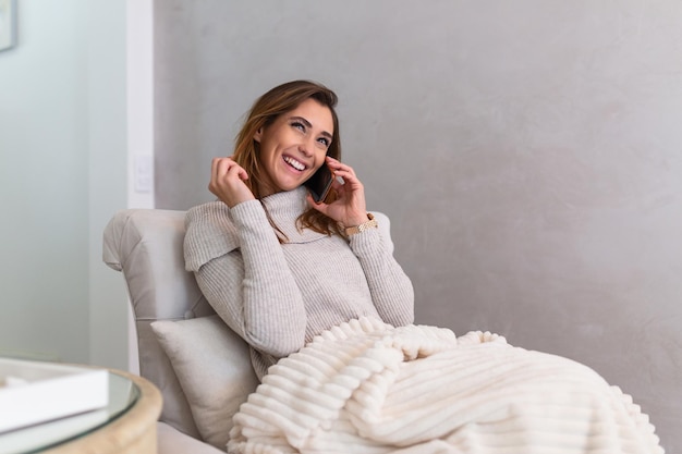 Buena mujer joven hablando por su teléfono móvil sentado en un gran sofá en casa. Hermosa chica hablando por teléfono inteligente en su acogedor apartamento