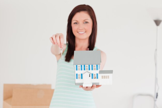 Foto buena mujer pelirroja sosteniendo una casa en miniatura mientras está de pie en el piso