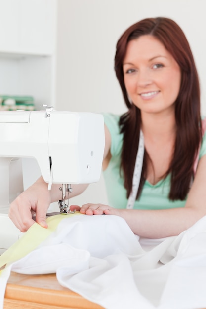 Buena mujer pelirroja usando una máquina de coser en la sala de estar