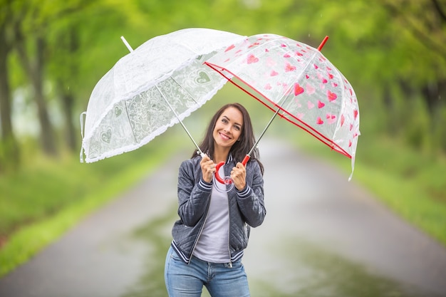 Buena mujer sostiene dos paraguas sobre ella bajo la lluvia durante un paseo por la naturaleza.