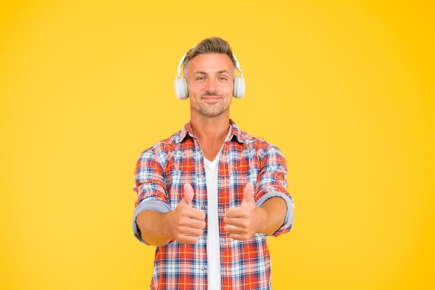 La buena música está a solo un par de auriculares de distancia El hombre feliz muestra su aprobación escuchando música de fondo amarillo Nueva tecnología Vida moderna Diversión y entretenimiento Alto y claro