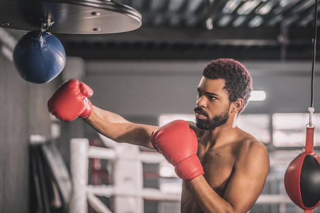 Una buena patada. Kickboxer afroamericano haciendo ejercicio en un gimnasio y pateando el saco de arena