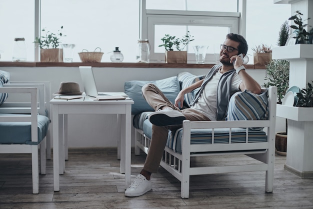 buena plática. Apuesto joven en gafas hablando por teléfono inteligente y sonriendo