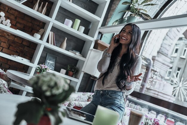 Buena plática. Atractiva joven mujer sonriente hablando por teléfono inteligente y gesticulando