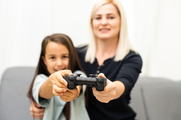 buena relación linda niña con madre joven usando joystick jugando videojuegos sentados juntos en la sala de estar disfrutando de unas vacaciones familiares.