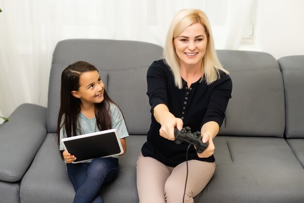 buena relación linda niña con madre joven usando joystick jugando videojuegos sentados juntos en la sala de estar disfrutando de unas vacaciones familiares.