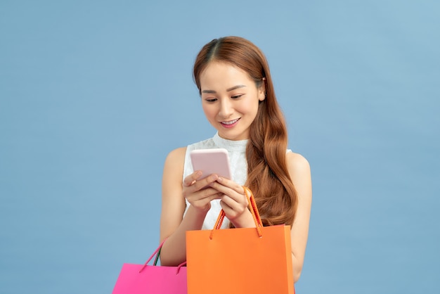 Buenas noticias y compras. Niña feliz sosteniendo bolsas con compras, sonriendo mientras mira el teléfono