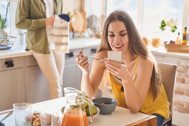 Buenas noticias. Persona muy femenina manteniendo una sonrisa en su rostro mientras toma un desayuno saludable. Concepto doméstico