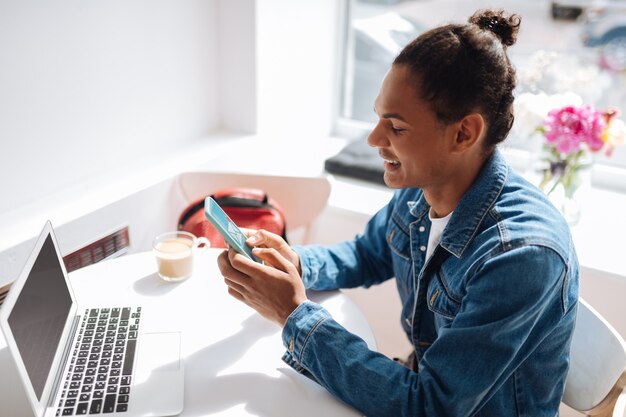 Foto buenas noticias. varón joven guapo manteniendo una sonrisa en su rostro mientras usa su gadget