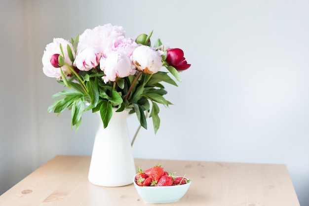 Bündel rosa Pfingstrosen in Vase und Erdbeere auf dem Holztisch.