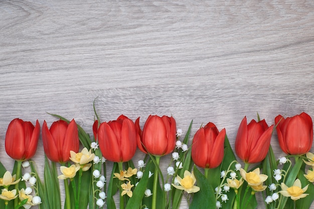 Bündel rote Tulpen, Narzissen und Maiglöckchen blüht auf hellem hölzernem Hintergrund