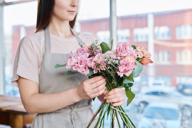 Bündel von frischen rosa Blumen gehalten von jungen zeitgenössischen Floristin, die über neuem Blumenstrauß arbeitet