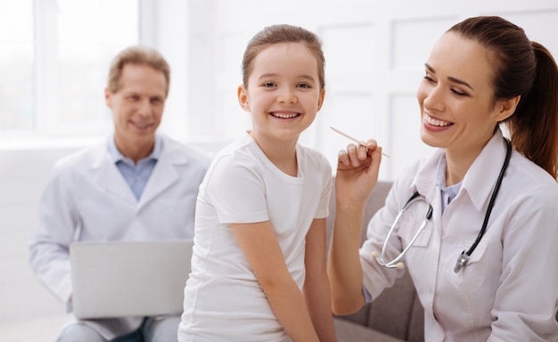 Foto buenos chicos. encantadora niña bonita sonriendo y mirando encantada mientras visita regularmente a su terapeuta