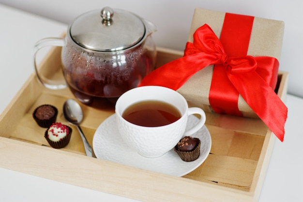 Buenos días concepto bandeja de madera con taza de té tetera dulces y caja de regalo en la mesa