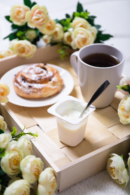 Buenos días - desayuno con bollo dulce, yogur y té en bandeja de madera