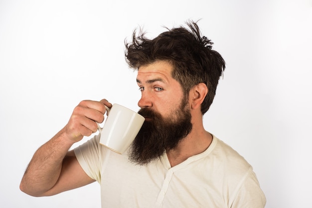 Buenos días guapo barbudo bebiendo una taza de bebida caliente por la mañana con café o leche hombre con