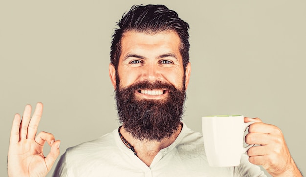 Buenos días, té hombre, está bien. Sonriente hombre inconformista con taza de café recién hecho, hombre feliz mostrando signo ok. Concepto de mañana.