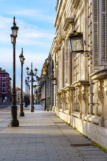 Bürgersteig der Straße des Königspalastes von Madrid mit Straßenlaternen und altem Gebäude am sonnigen Tag. Spanien.