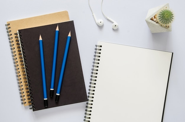 Büro Arbeitsplatzkonzept. Notizbuch, Kaktus, Kopfhörer und Bleistift auf weißem Schreibtisch.
