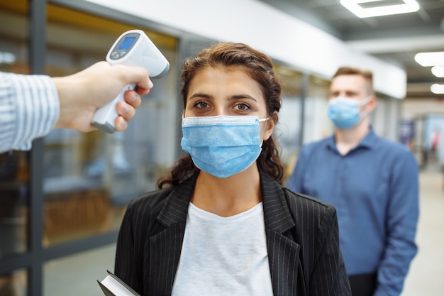 Büroangestellte werden während einer Pandemie mit einem entfernten berührungslosen Thermometer überprüft