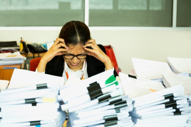 Büroangestellte wird mit viel Schreibarbeit auf ihrem Schreibtisch beunruhigt.