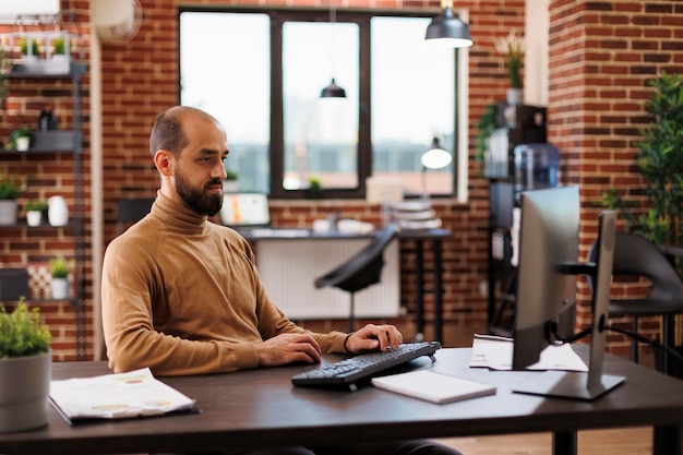 Büroangestellter einer Geschäftsentwicklungsagentur, der im Arbeitsbereich sitzt, während er den Computer benutzt. Finanzberater eines Marketingunternehmens, der an einem Managementplan für ein Startup-Projekt arbeitet.