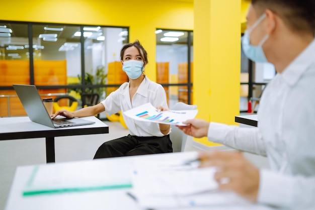Büroangestellter mit Gesichtsmaske zur sozialen Distanzierung zur Virenprävention bei der Verwendung eines Laptops