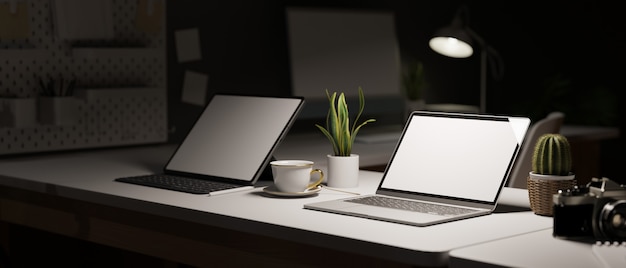 Büroarbeitsplatz im dunklen Stil in der Nacht mit zwei Laptops mit leerem Bildschirm auf dem Schreibtisch