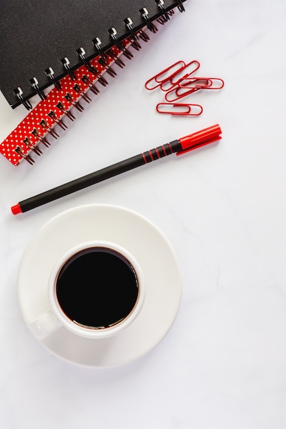 Bürobedarf mit Spiralblock, Stift, Büroklammern und eine Tasse schwarzen Kaffee