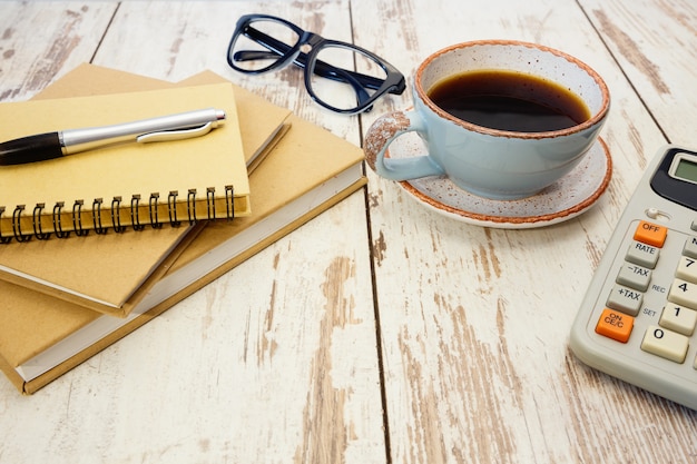 Bürobedarf, Notizblöcke, Taschenrechner und eine Tasse Kaffee auf einem Retro-Holztisch.