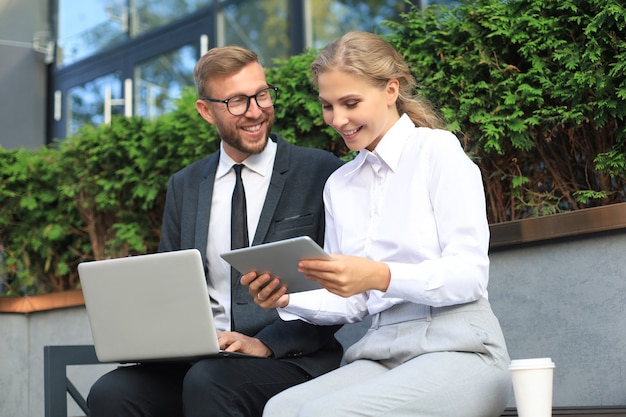 Bürokollegen mit Laptop-Computer beim Sitzen auf einer Bank im Freien.