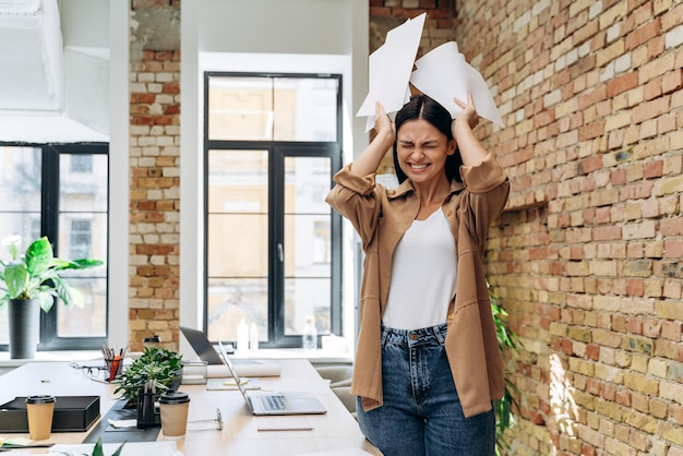 Büroporträt einer schönen unzufriedenen Geschäftsfrau, die nach gestresster Arbeit wütend Dokumente hält und schreit