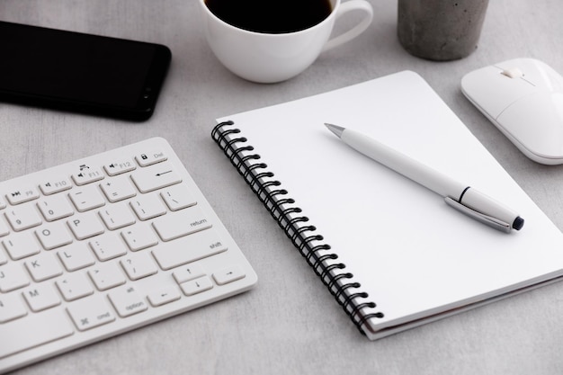 Bürotisch mit Notebook, Kaffeetasse, Tastatur, Maus und Handy auf Marmorhintergrund.