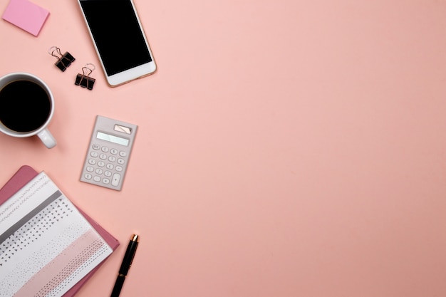 Bürotisch Schreibtisch mit Smartphone und anderen Büromaterial auf rosa Hintergrund.