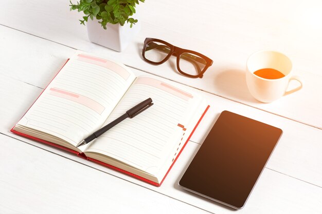 Bürotisch Schreibtisch mit Zubehör, weißer leerer Notizblock, Tasse, Stift, Tablet, Brille, Blume auf weißem Hintergrund. Draufsicht und Platz für Text kopieren