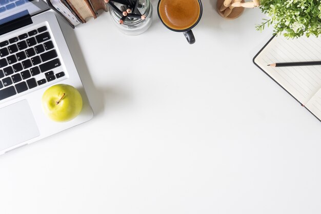 Bürotischlaptop, Notizbuchpapier, Bleistift, Buch und Kaffee auf weißem Tabellenarbeitsplatz.