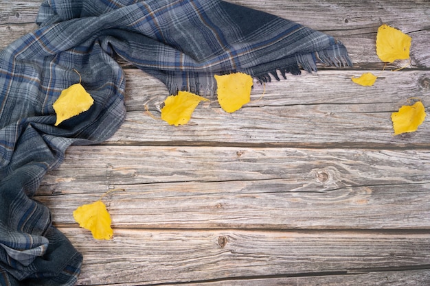 Foto bufanda gris y hojas secas de color amarillo sobre la superficie de la madera